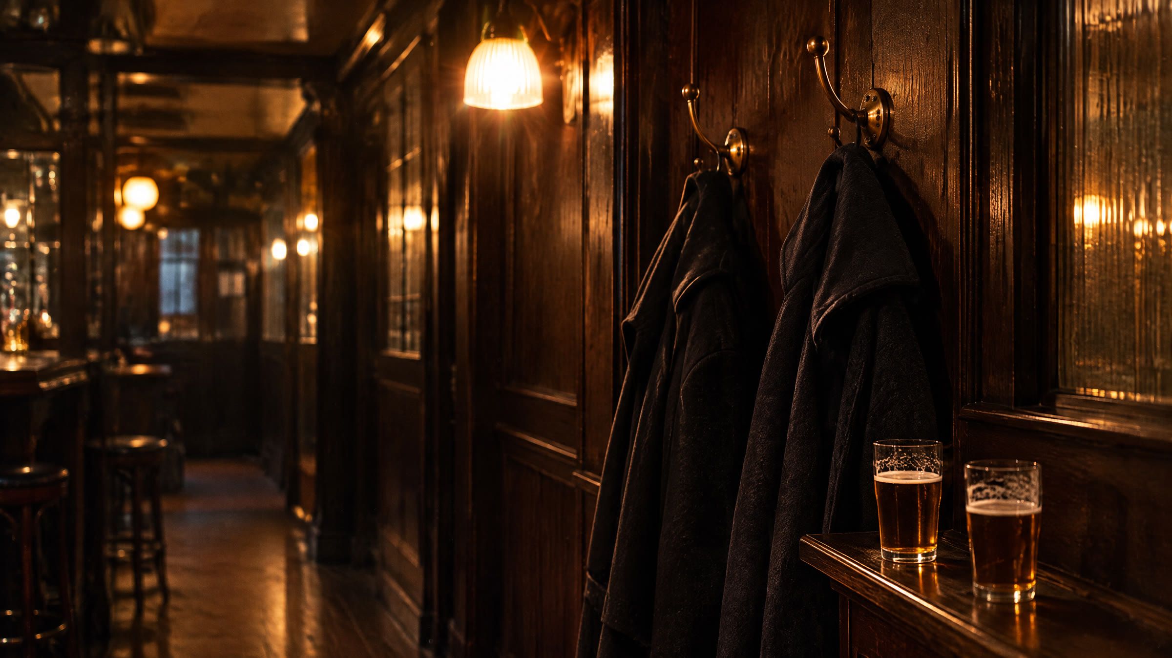 To mørke uldfrakker på knager ved siden af hinanden i en bars gang, to fadøl på en hylde nedenunder.